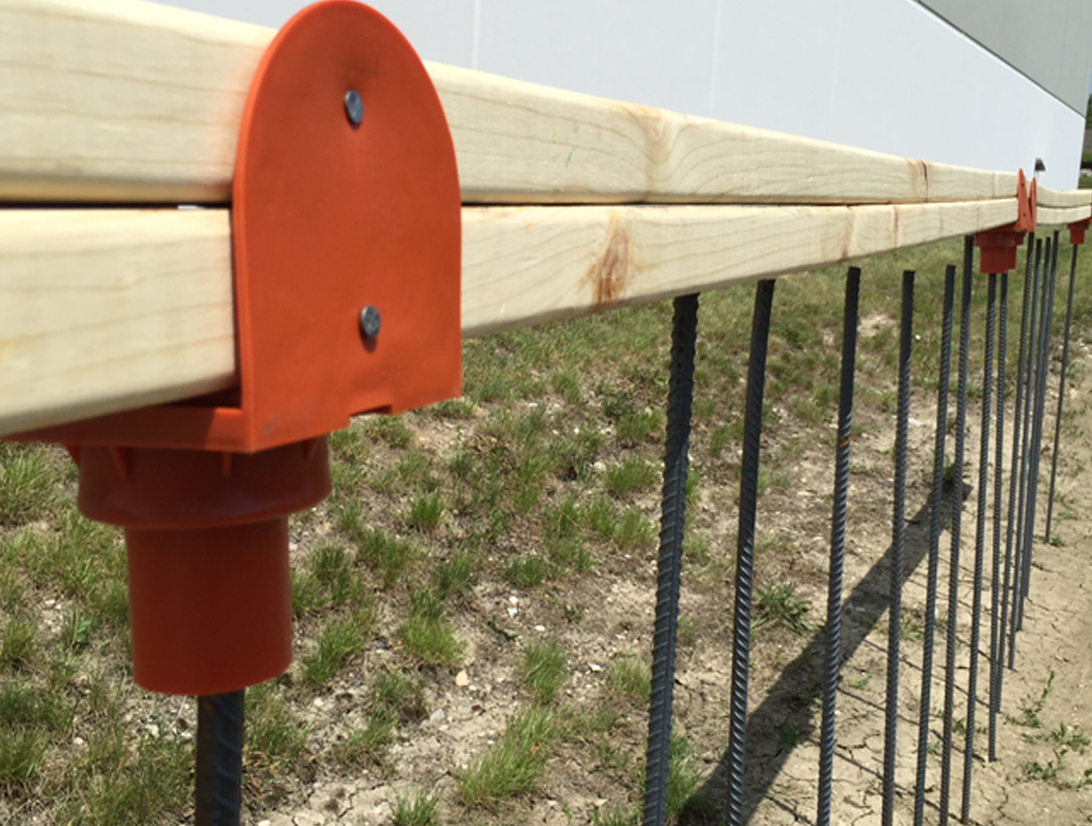Close-up of a wooden guardrail system secured with a Protective Cover Adapter mounted on exposed rebar at a construction site.
